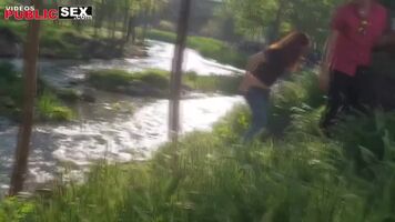 Girl at festival bends over and pees forcefully into the grass by the river